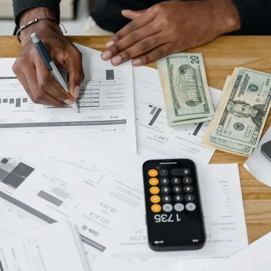Accountant's hands writing on financial reports next to a calculator, cash and laptop at a Perth practice — Systemly builds automated client reminder systems for accounting practices