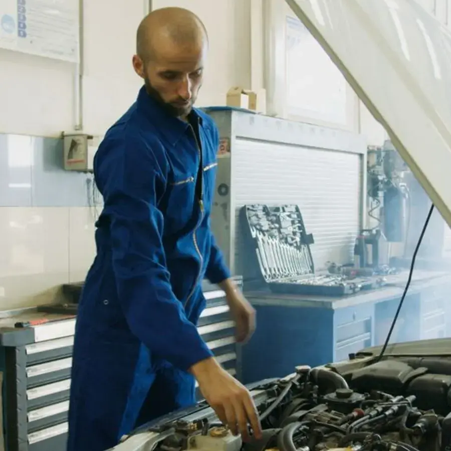 Mechanic in blue overalls inspecting a car engine in a Perth workshop — Systemly builds automated booking and service reminder systems for auto repair shops