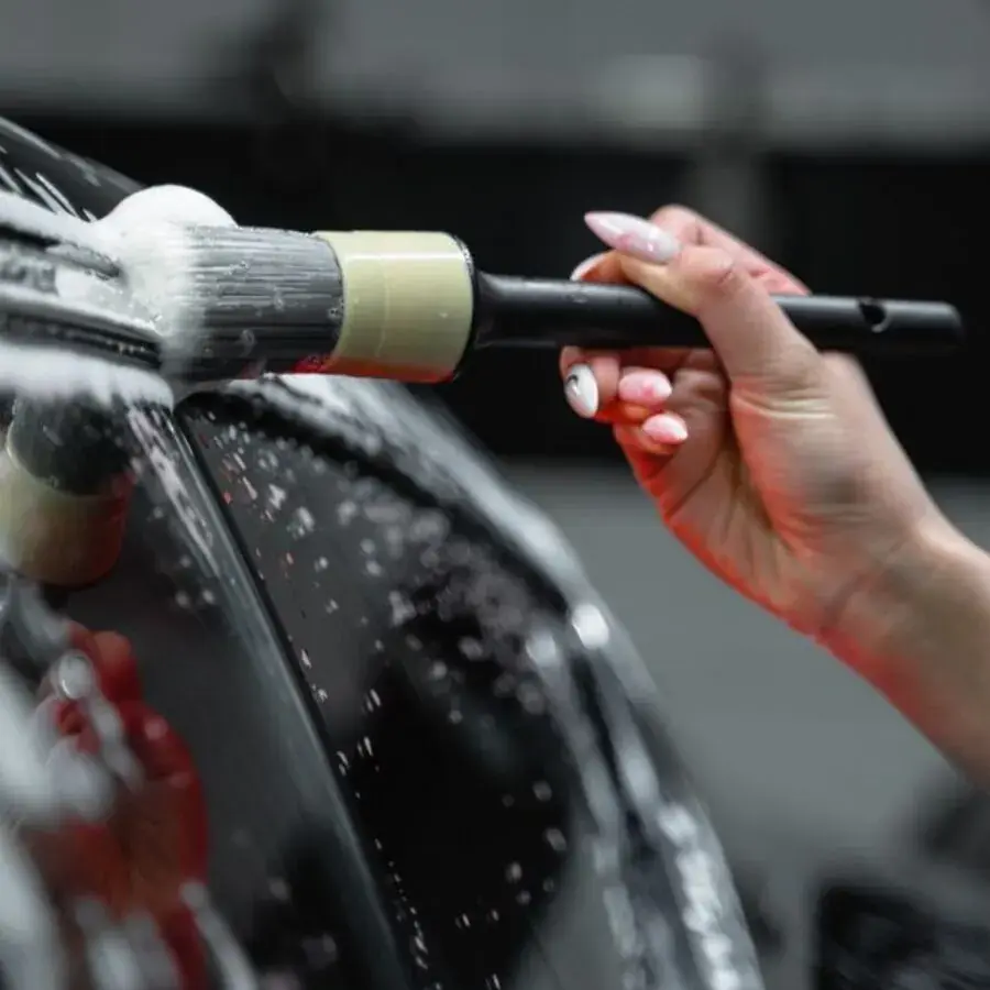 Detailer's hand using a foam-tipped brush to clean a black car panel at a Perth detailing studio — Systemly builds automated booking and review systems for car detailing businesses