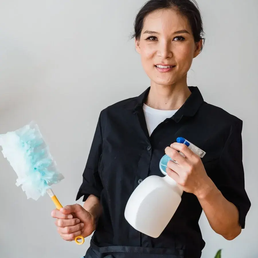 Smiling professional cleaner holding a duster and spray bottle indoors — Systemly builds automated booking and rebooking systems for cleaning businesses