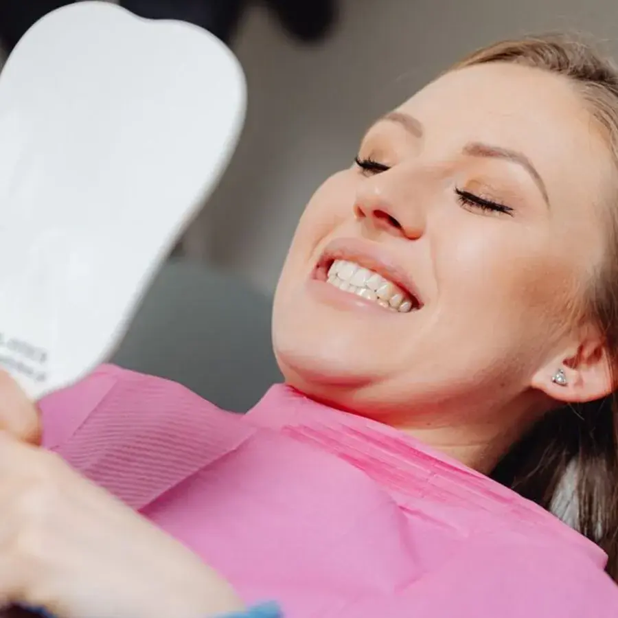 Smiling dental patient checking her smile in a hand mirror at a Perth clinic — Systemly builds automated booking and reminder systems for dental practices