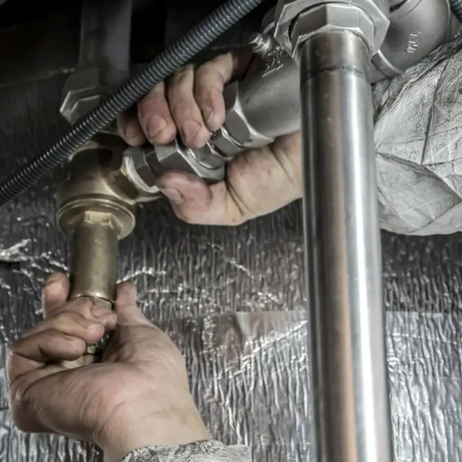 Perth plumber's hands fitting a pipe joint under a sink — Systemly builds automated call answering and booking systems for plumbing businesses